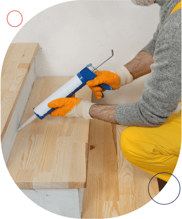 A person applying caulk to seal the joint between wooden stairs.